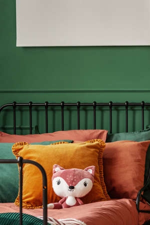 Close-up of a plush fox toy on a bed with orange sheets and cushions in a bedroom interior for a...