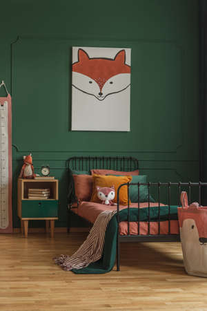 Cute fox painting hanging on a dark green wall in a child bedroom interior with metal bed, orange sheets and wooden bedside cabinet. Real photoの写真素材