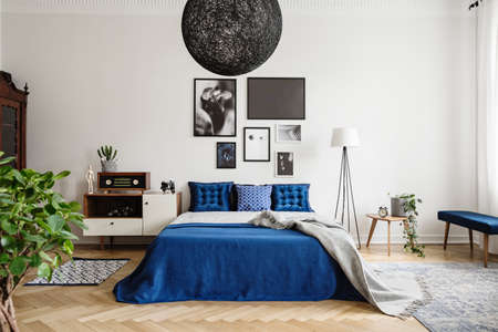 Black chandelier in navy blue bedroom in tenement house. Floor lamp between king size bed and small...