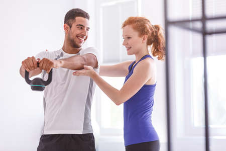 Smiling sportsman with weight during workout with personal trainer