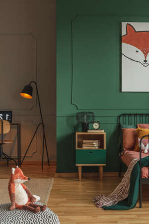 Real photo of a kids room interior with a black lamp between a desk with laptop and bed with green blanketの写真素材
