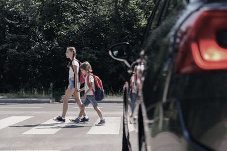 Low angle on car in front of children with backpacks walking through crosswalk to the schoolの写真素材