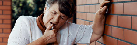 Elderly lady leaning against a brick wall of her home having heart problemsの写真素材