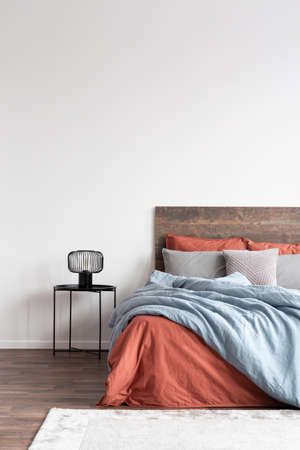 Minimal cozy interior with wooden bed with natural bedclothes on the empty white wallの写真素材