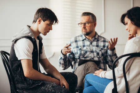 Sad teenager listening to his psychatrist during visit in mental hospital with his mother