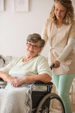 Positive senior patient on wheelchair with supportive nurse