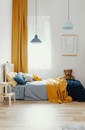 Teddy bear on single wooden bed in blue and orange bedroom interiorの写真素材