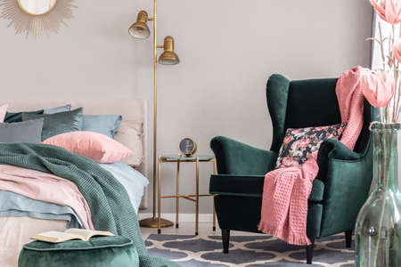 Floral pillow and pink blanket on emerald green comfortable armchair in fashionable bedroomの写真素材