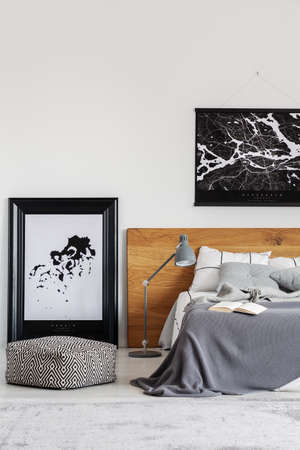 Black map on white wall above wooden headboard in simple bedroom interiorの写真素材