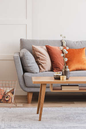 Cotton flower on stylish copper vase on small wooden coffee table next to grey setteeの写真素材
