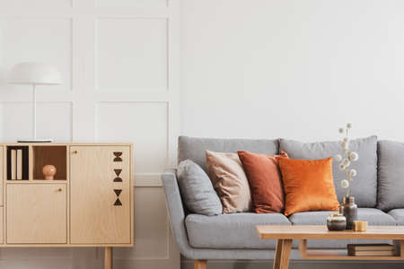 Vintage wooden commode next to grey Scandinavian sofa with pillowsの写真素材