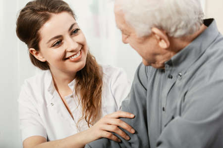 Beautiful volunteer smiling at senior man at nursing homeの写真素材
