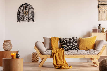 Scandinavian sofa with pillows and dark yellow blanket in bright living room interior with black chandelierの写真素材