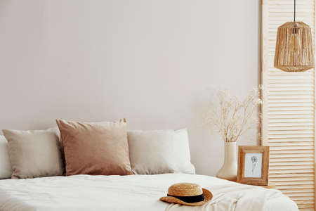 Natural fashionable bedroom interior with wicker hat on white beddingの写真素材