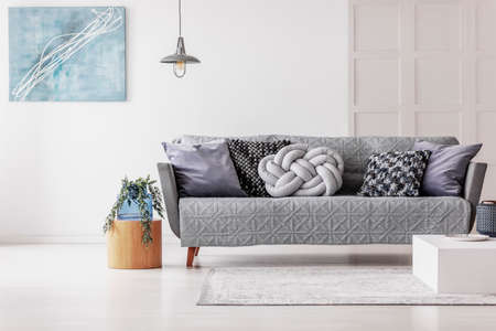 Green flowers in blue glass vase on wooden table next to grey sofa with pillowsの写真素材