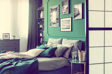 Champagne and glasses on nightstand table next to king size bed with luxurious bedding in elegant...