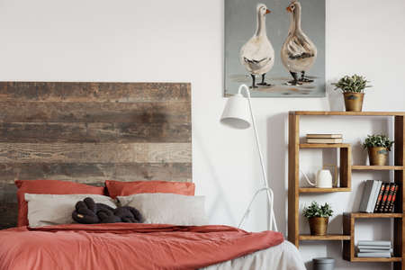 Comfortable king size bed with wooden rustic headboard and white industrial lamp next to itの写真素材