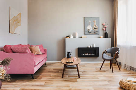 Stylish living room interior with pastel pink sofa, wooden coffee table and eco fireplaceの写真素材