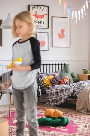 Blurred blonde kid standing in colorful bedroom full of design furniture and toysの写真素材