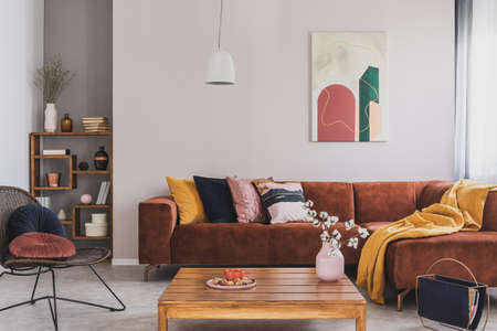 Flowers in vase on wooden coffee table in fashionable living room interior with brown corner sofa...