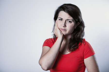 Pretty young student woman with a aching tooth, copy space on empty backgroundの写真素材