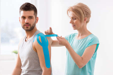 Physiotherapist covering selected fragments of young man's body with special structure patches...