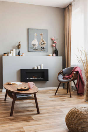 Cookies and pink team mug on wooden coffee table in grey living room interior with eco fireplace and chic chairの写真素材