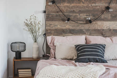 Real photo of a cozy, pink bedroom interior for a girl with lights hanging on a wooden bedheadの写真素材