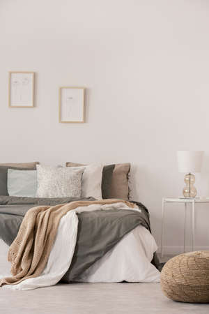 Stylish white lamp on simple nightstand table next to warm bed with cozy grey beddingの写真素材