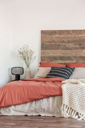 Cozy bedroom interior with white walls, wooden bedhead and red sheets. Real photoの写真素材