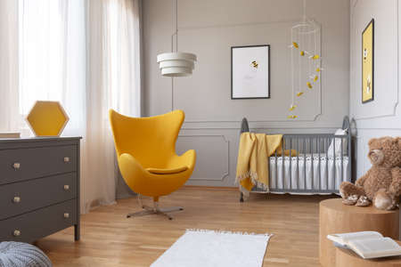 Trendy yellow egg chair in elegant grey nursery with wooden crib and posters on the wallの写真素材