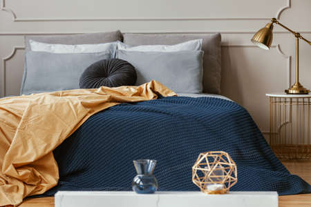 Golden lamp on trendy nightstand next to king size bed with comfortable bedding