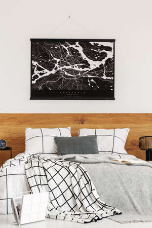 Black map on white wall above wooden headboard in simple bedroom interior