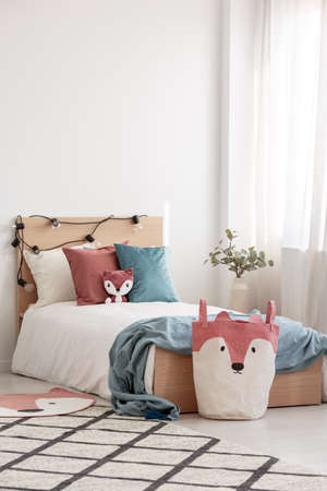 Velvet pastel pink and turquoise pillows and toy fox on single wooden bed with white bedding and...