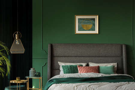Stylish poster above comfortable king size bed with headboard in dark green bedroomの写真素材