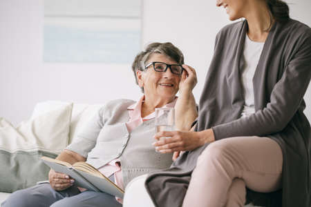 Older woman reading a book together with young caregiverの写真素材
