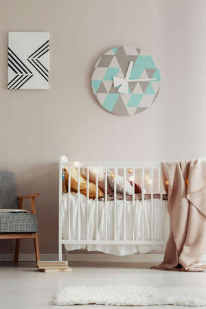 Cute, scandi bedroom interior for a child with a white crib, pastel wall and a round clock. Real photoの写真素材