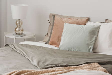 Close up of stylish lamp on white nightstand next to king size bed with pillows and duvet