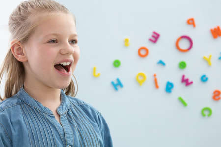 Cute blond little girl opening her mouth during speech therapy, copy space on the wall with lettersの写真素材