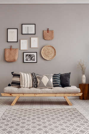 Dry flowers in white vase on small wooden table behind comfortable futon sofa with pillowsの写真素材