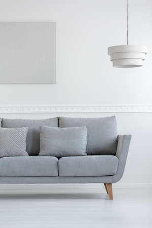 Scandinavian living room sofa in white daily room interior with painting on the wall and lamp aboveの写真素材
