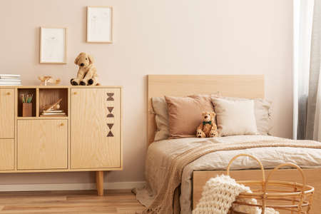 Stylish wooden commode with plush toy on top next to single bed in kid's bedroomの写真素材
