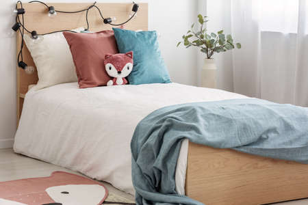 Velvet pastel pink and turquoise pillows and toy fox on single wooden bed with white bedding and...