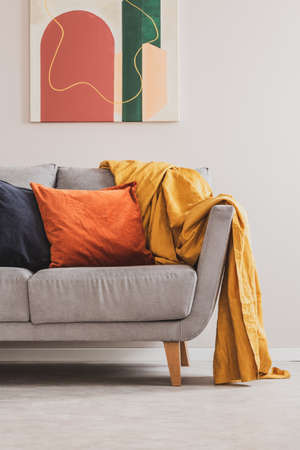 Yellow blanket on grey sofa with orange and black pillowsの写真素材