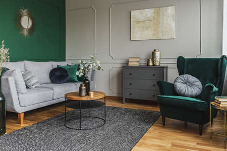 Emerald green wing back chair with pillow in grey living room interior with wooden commodeの写真素材