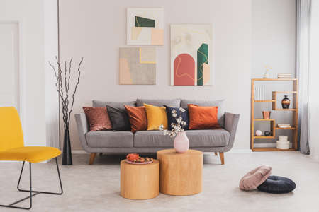 Yellow, orange, black and brown pillows on comfortable grey scandinavian sofa in bright living room interior with abstract paintings on the wallの写真素材