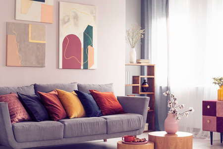 Yellow, orange, black and brown pillows on comfortable grey scandinavian sofa in bright living room interior with abstract paintings on the wallの写真素材