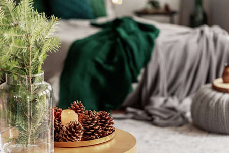 Spruce candle and cone on small wooden table in grey and emerald green bedroom interior
