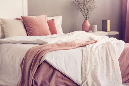 King size bed with pastel pink and white bedding in trendy bedroom interiorの写真素材