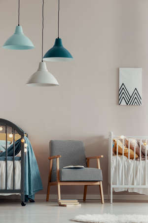Pastel lamps above stylish vintage armchair in the middle of cute baby room for twinsの写真素材